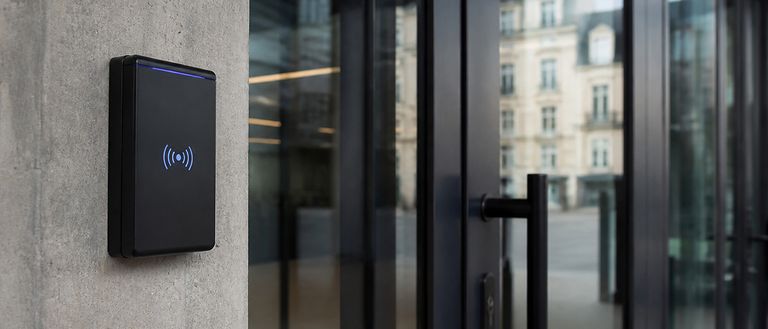 Lecteur de badge sans contact à côté de la porte vitrée d'un immeuble
