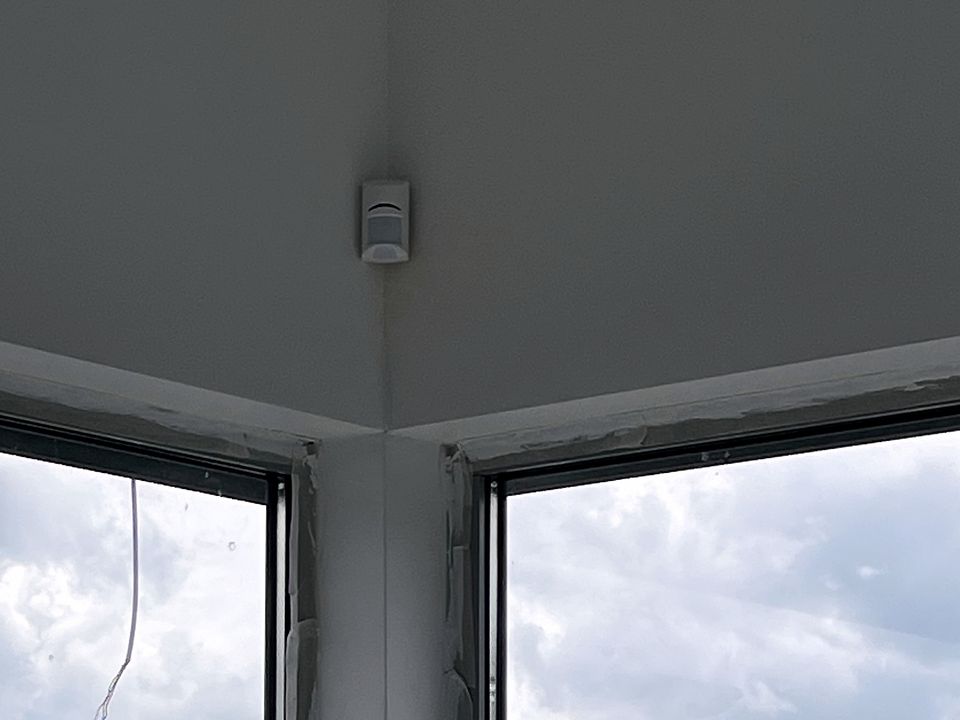 Détecteur de mouvement posé dans un angle de plafond, au-dessus de grandes baies vitrées